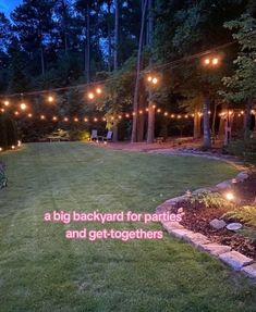 a backyard with lights strung over the grass and trees in the background at night time