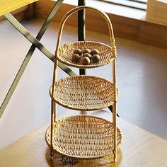 a three tiered wicker basket on top of a wooden table next to a window