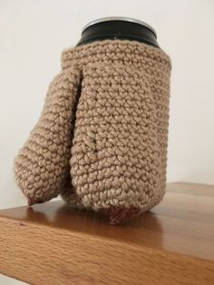 a crocheted coffee cup cozys up on a wooden shelf with a black lid