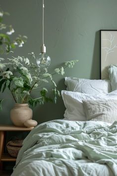 a bedroom with green walls and white linens on the bed, potted plants in the corner