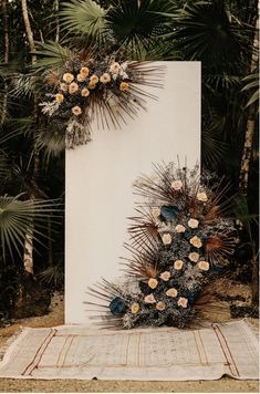 a white sign with flowers on it sitting in front of some palm trees and bushes