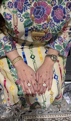 a woman sitting down with her hands on her knees, wearing rings and bracelets