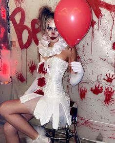 a woman dressed in white holding a red balloon with blood on the wall behind her