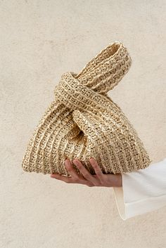 a hand holding a gold knitted bag with a knot on the front and side