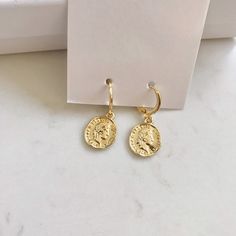 Dainty gold dangle coin earrings. These gold huggie earrings feature a tiny Italian lira coin charm. Delicate and yet eye catching. The ultimate accessory for every outfit, day to night. made of 14k gold plating over brass. Measurements: Diameter- 10mm Coin charm- 12xmm Shipping: Please allow 1-3 business days for your order to be processed and shipped. All orders are shipped in our customize box, gift ready. *Let me know if you have any questions and I will promptly respond 14k Gold Filled Charms Drop Earrings, Gold Drop Earrings With Charms, 14k Gold Filled Drop Earrings With Charms, Nickel Free Gold Plated Circle Earrings, Nickel-free Gold Plated Circular Earrings, Nickel-free Gold-plated Circular Earrings, Tarnish Resistant Circular Earrings As Gift, Tarnish Resistant Circular Earrings For Gifts, Round Tarnish Resistant Earrings For Gift