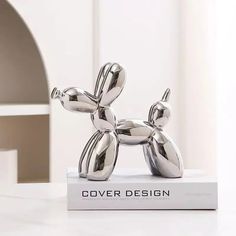 a silver balloon dog statue sitting on top of a book