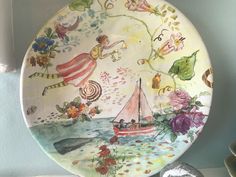 a decorative plate with an image of a boat on the water and flowers painted on it