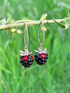 two small blackberries with red berries hanging from them on a branch in front of some green grass