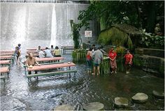 people are standing in the water near picnic tables under a waterfall at an amusement park