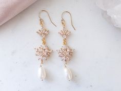 a pair of gold - tone earrings with white pearls and crystal beads on a marble surface