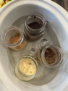 four jars filled with food sitting on top of a white plate next to corn kernels