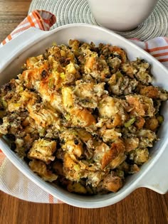 a casserole dish filled with stuffing on top of a wooden table next to a white bowl