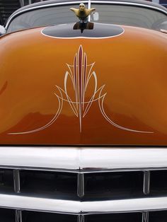 the front end of an orange car with a bird decoration on it's hood