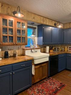 a kitchen with blue cabinets and wooden counter tops on a rug in front of the sink