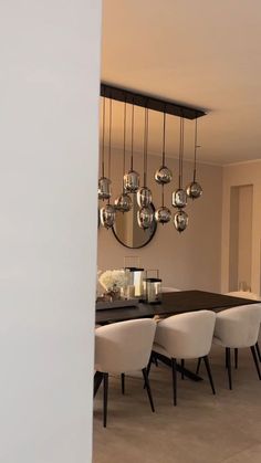 a dining room table with white chairs and a large round mirror hanging from the ceiling