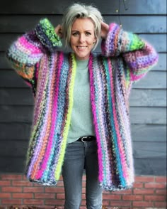 a woman standing in front of a brick wall wearing a multicolored cardigan