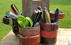 several different types of knives in leather cups on a wooden table with grass behind it