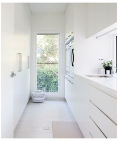 a long narrow white kitchen with an open window on the side and a washer and dryer in the middle