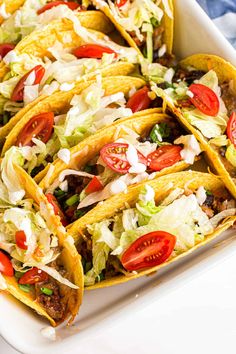 tacos filled with meat, lettuce and tomatoes on a white platter