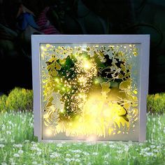 a lit up box sitting on top of a lush green field next to flowers and trees