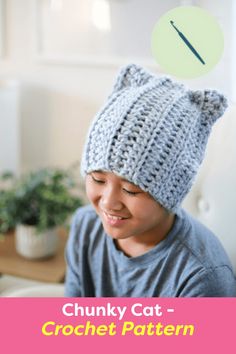 a young boy wearing a knitted cat hat while sitting on a couch in front of a plant