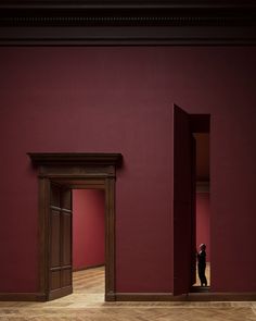 an empty room with red walls and two doors, one person standing in the doorway