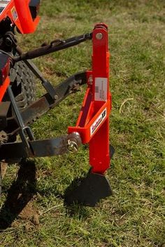 an orange and black mower sitting on top of a grass covered field next to a fork