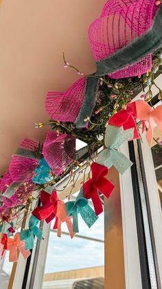 some pink and blue paper flowers hanging from the ceiling in front of a window with a sky background