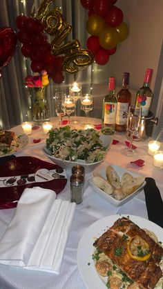 a table topped with plates of food next to wine glasses and balloons in the background