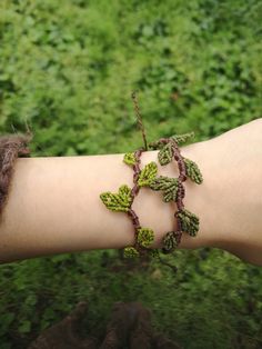 a woman's arm is adorned with green leaves and brown cords that are attached to the wrist