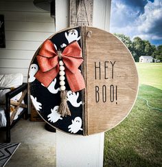 a wooden sign that says hey boo hangs on the side of a house with halloween decorations