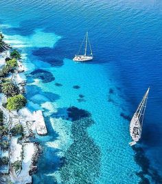 two boats floating in the blue water next to some sand and trees on the shore