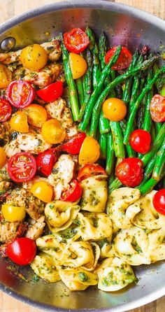 a pan filled with pasta, asparagus and tomatoes