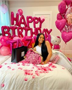 a woman sitting on top of a bed with pink balloons in the shape of hearts