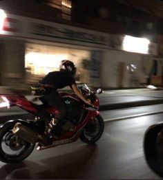 a man riding on the back of a red motorcycle down a city street at night