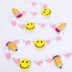 some smiley faces are made out of plastic beads on a white surface with pink and yellow balls around them