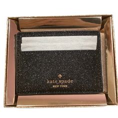 a black and gold card case with a white stripe on the front that says kate spade new york