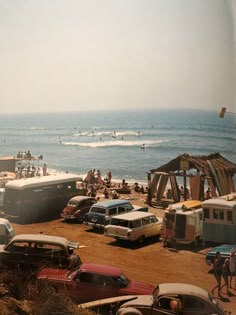 many cars are parked on the beach by the ocean and people in the water behind them