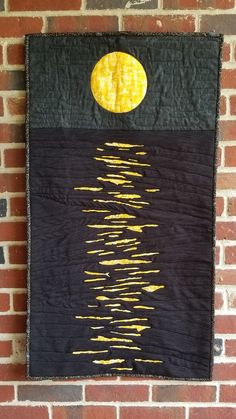 a black and yellow wall hanging on a brick wall with the moon in the sky