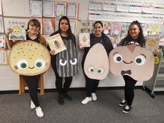 four girls are holding up paper cutouts with faces on them in front of a bulletin board