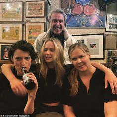 three women and a man are posing for the camera with a beer in front of them