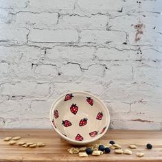 a bowl with strawberries and blueberries on it sitting on a wooden table next to a brick wall