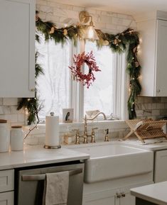 a kitchen decorated for christmas with wreaths and garland on the window sill, candles in front of the sink