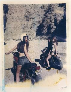 two women are sitting on motorcycles in the sand and one is wearing a cowboy hat