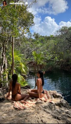 two women in bikinis sitting on rocks near water