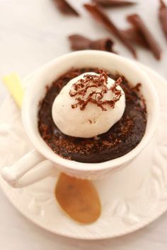 a cup filled with ice cream and chocolate sauce on top of a white plate next to pieces of chocolate