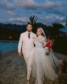 a bride and groom are walking down the path at their outdoor wedding ceremony in front of a pool