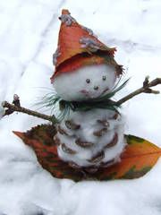 a snowman is sitting in the snow wearing a hat and holding a branch with leaves