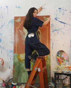 a woman in overalls is painting on the wall