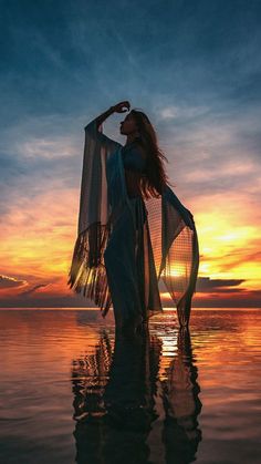 a woman standing in the water with her arms around her neck and wearing a sheered shawl